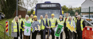 Group of people in high-vis holding EV-related cardboard cutouts in front of a bus