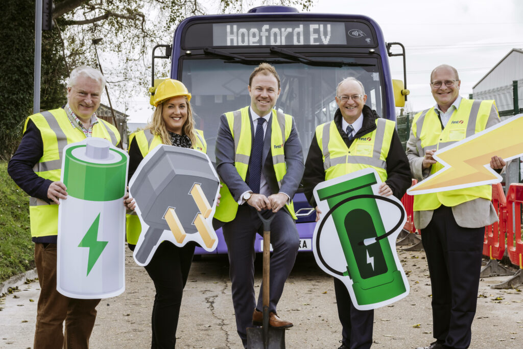 Five people in high-vis holding EV-related cardboard cutouts in front of a bus